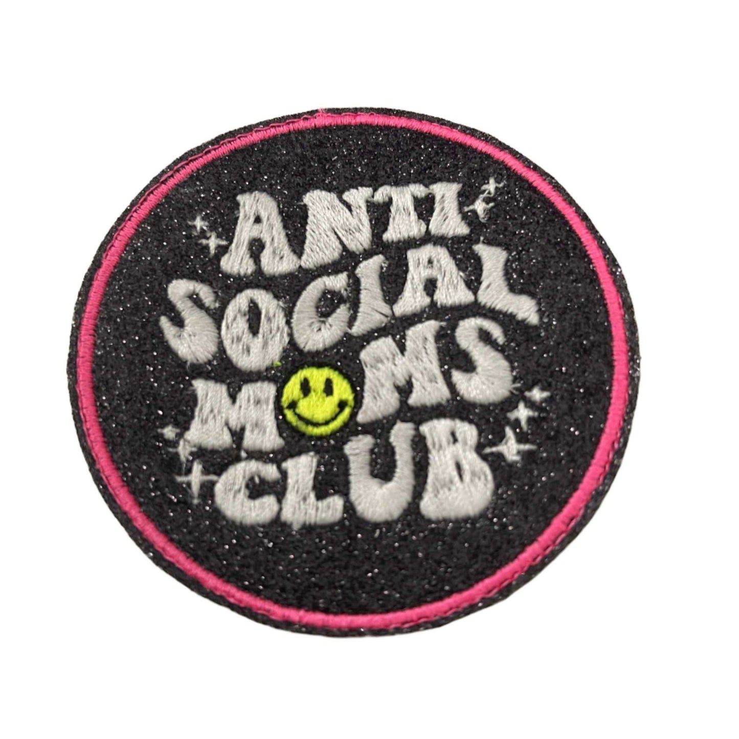 Anti solcial moms club patch with neon yellow smiley and pink outline on black glitter background.