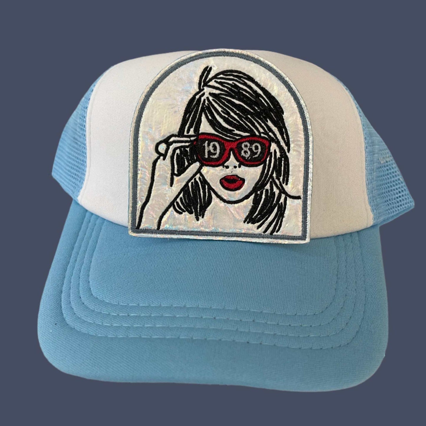Iron-on patch featuring a black and white illustration of Taylor Swift with red sunglasses marked "1989" on a holographic silver background, outlined in black.