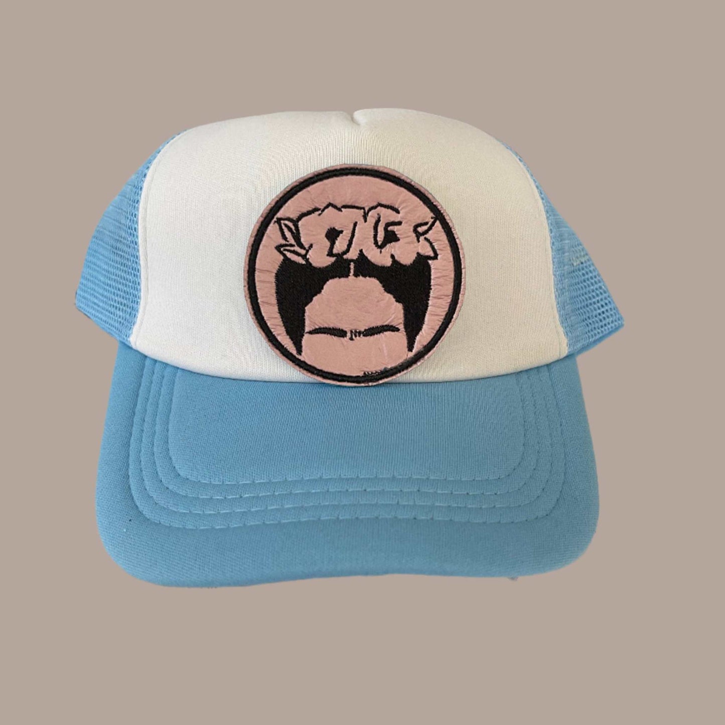 Iron-on patch featuring a black and pink illustration of Frida Kahlo's face and hair with her signature flower crown, enclosed within a circular black border.