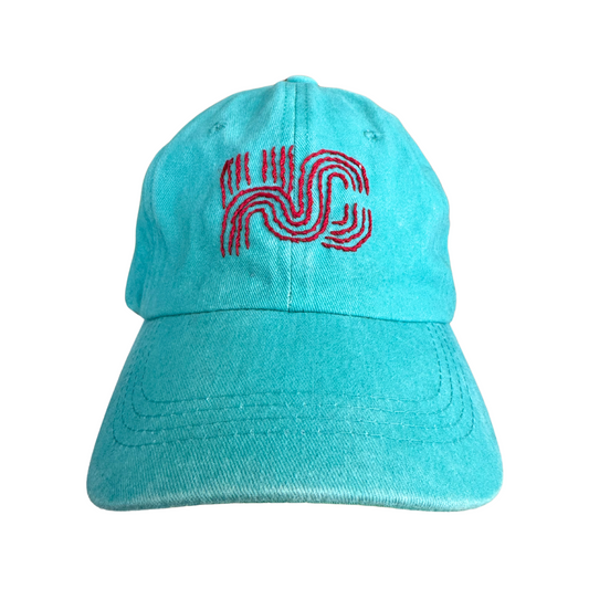 Hand-embroidered KC Current colors hat with original Milkweed Baby KC logo on teal background.