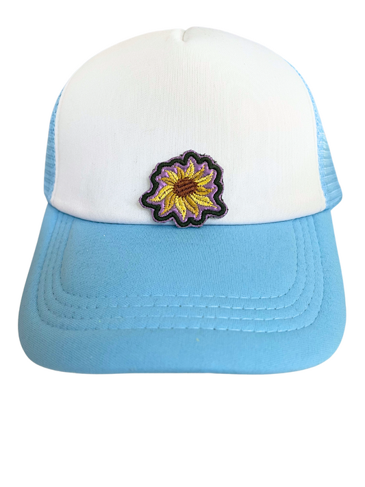 Close-up of a handmade sunflower patch with intricate embroidery, showcasing vibrant yellow petals and a background that changes from green to purple depending on the light.