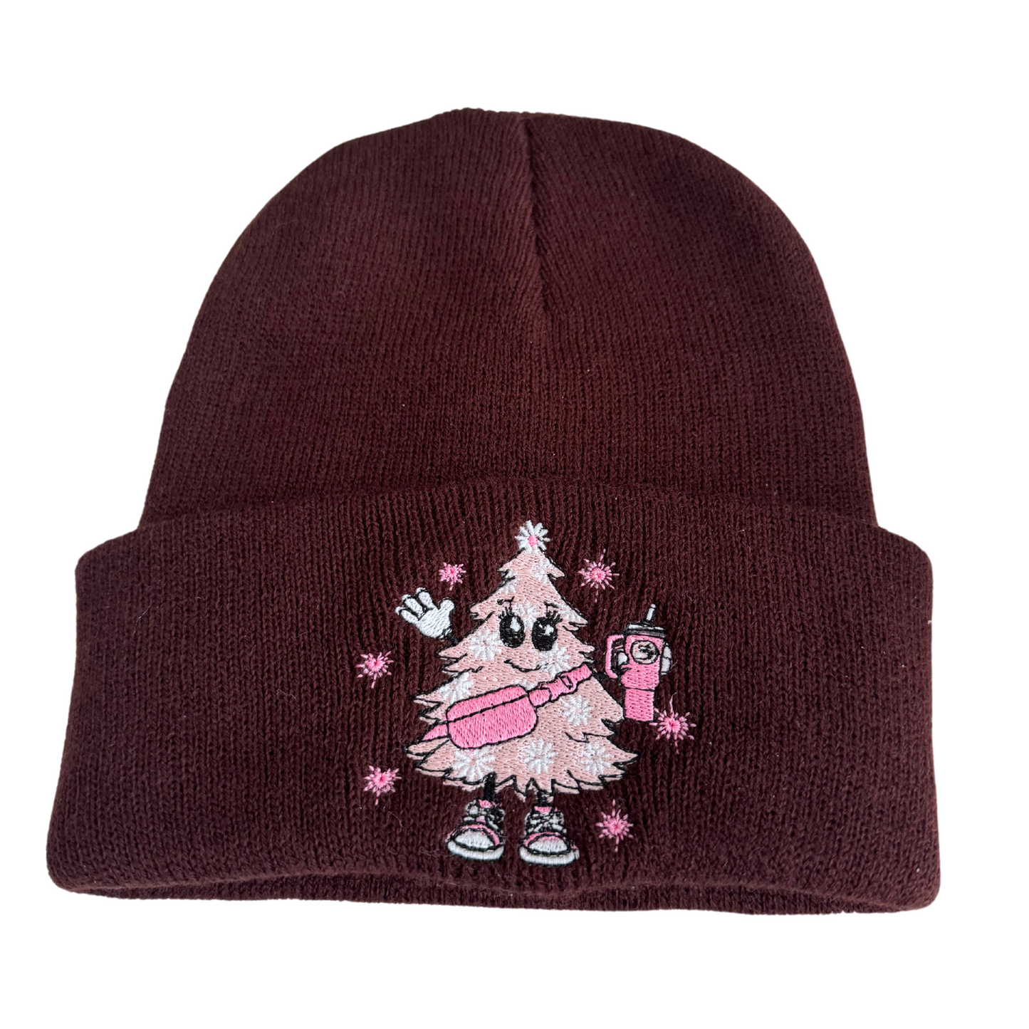 Brown beanie with a pink Christmas tree embroidery wearing sneakers and holding a festive drink.