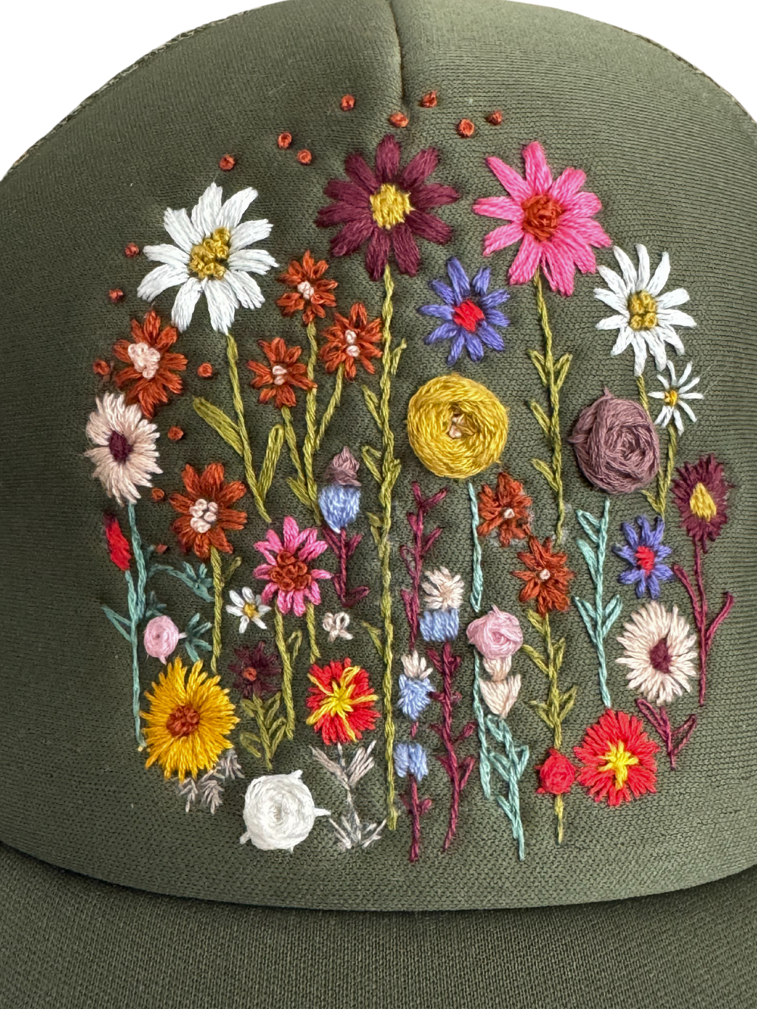 Close-up of hand-embroidered wildflower field design on an olive green trucker hat.