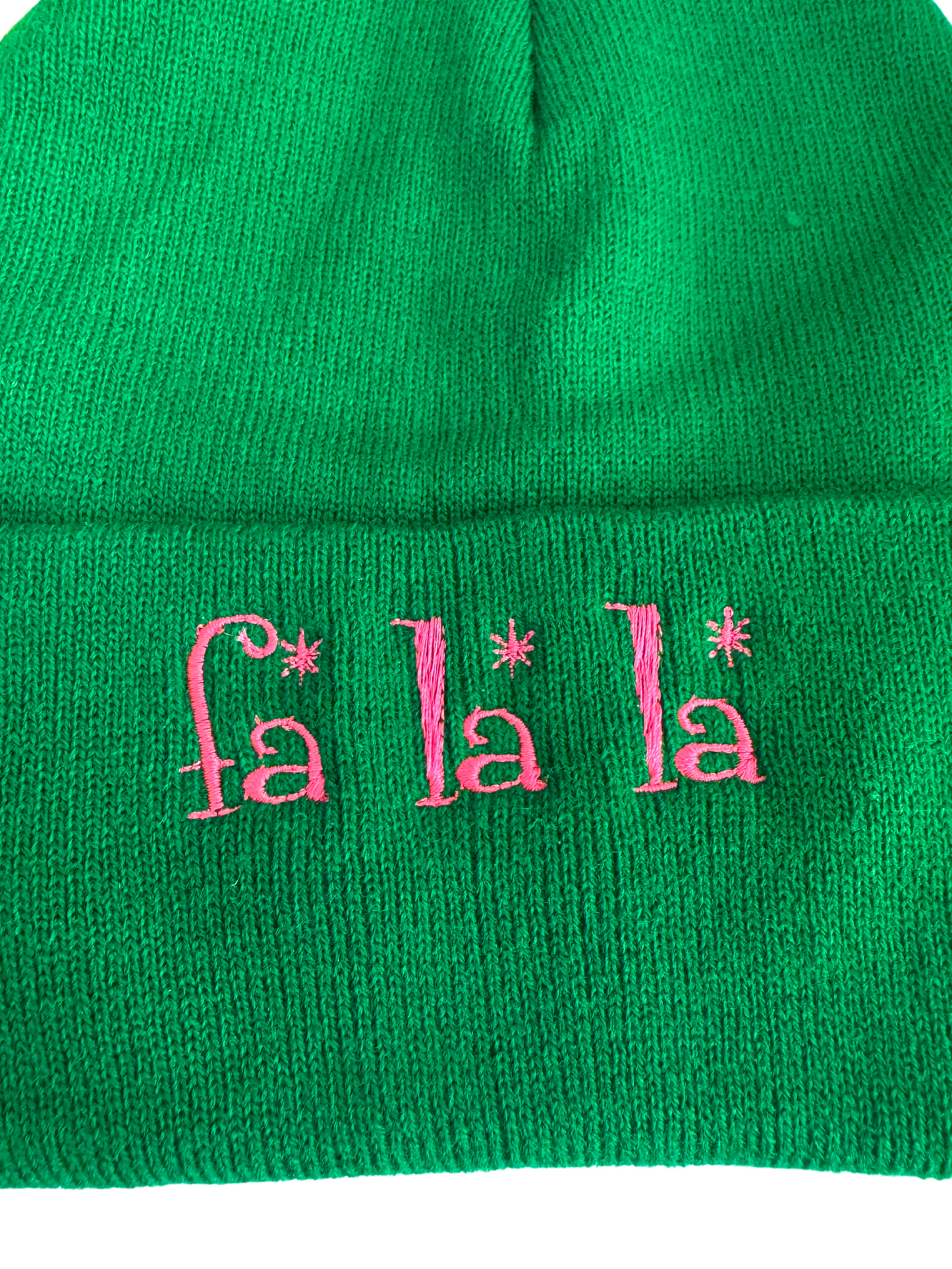 Green beanie with pink "Fa La La" embroidered text, festive winter holiday theme.