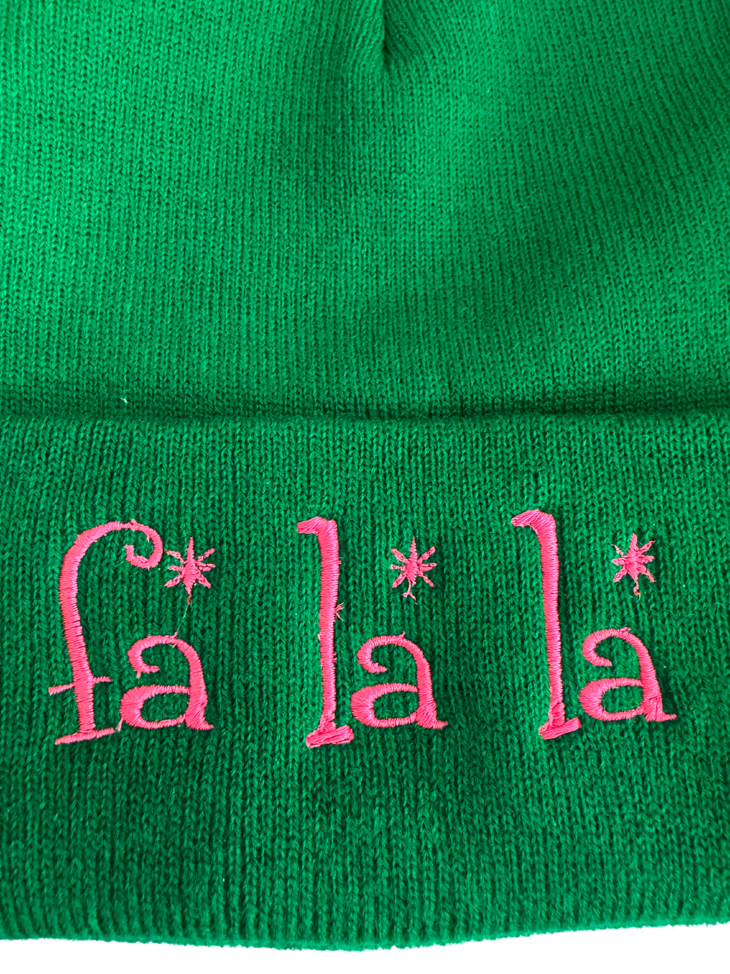 Green beanie with pink embroidered "Fa La La" design featuring whimsical fonts and festive charm.