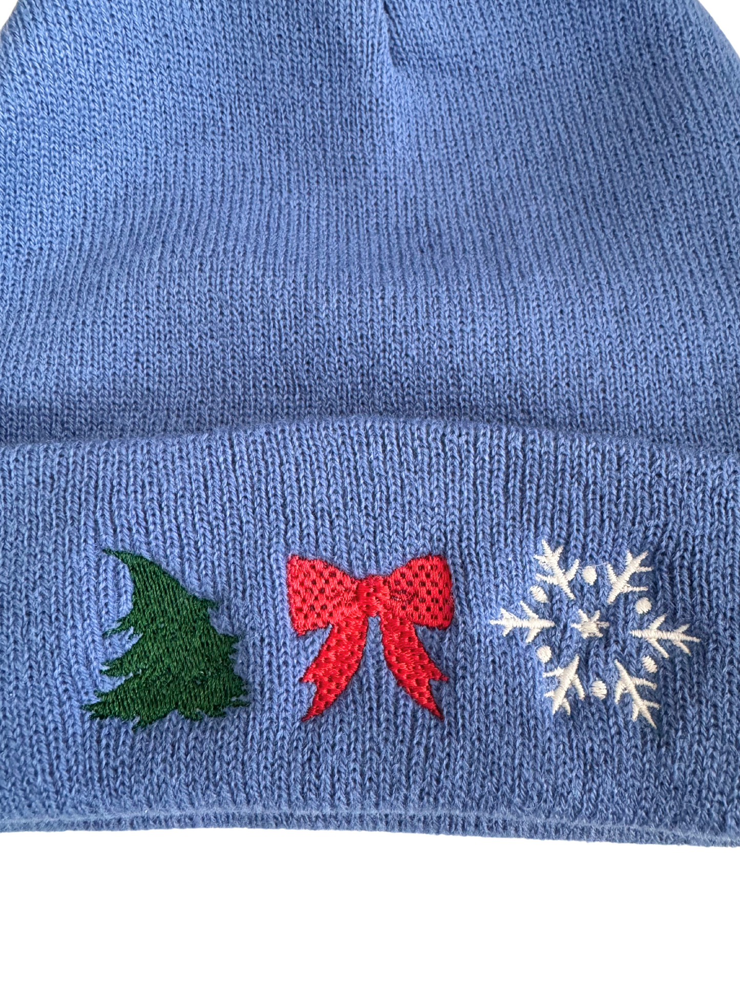 Blue holiday beanie with machine-embroidered Christmas tree, red bow, and snowflake designs.