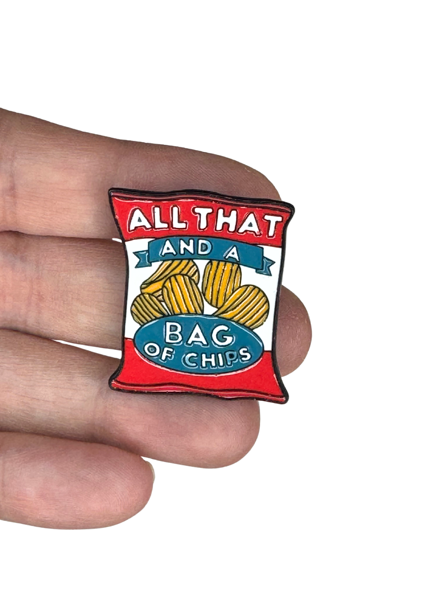 Hand holding the enamel pin shaped like a chip bag with bold retro design.