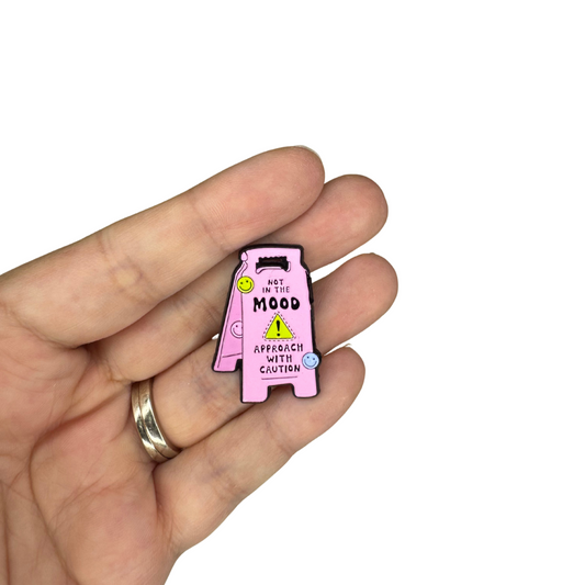 Enamel pin held in hand for scale reference