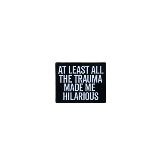 Hero image of black enamel pin reading “At Least All the Trauma Made Me Hilarious”