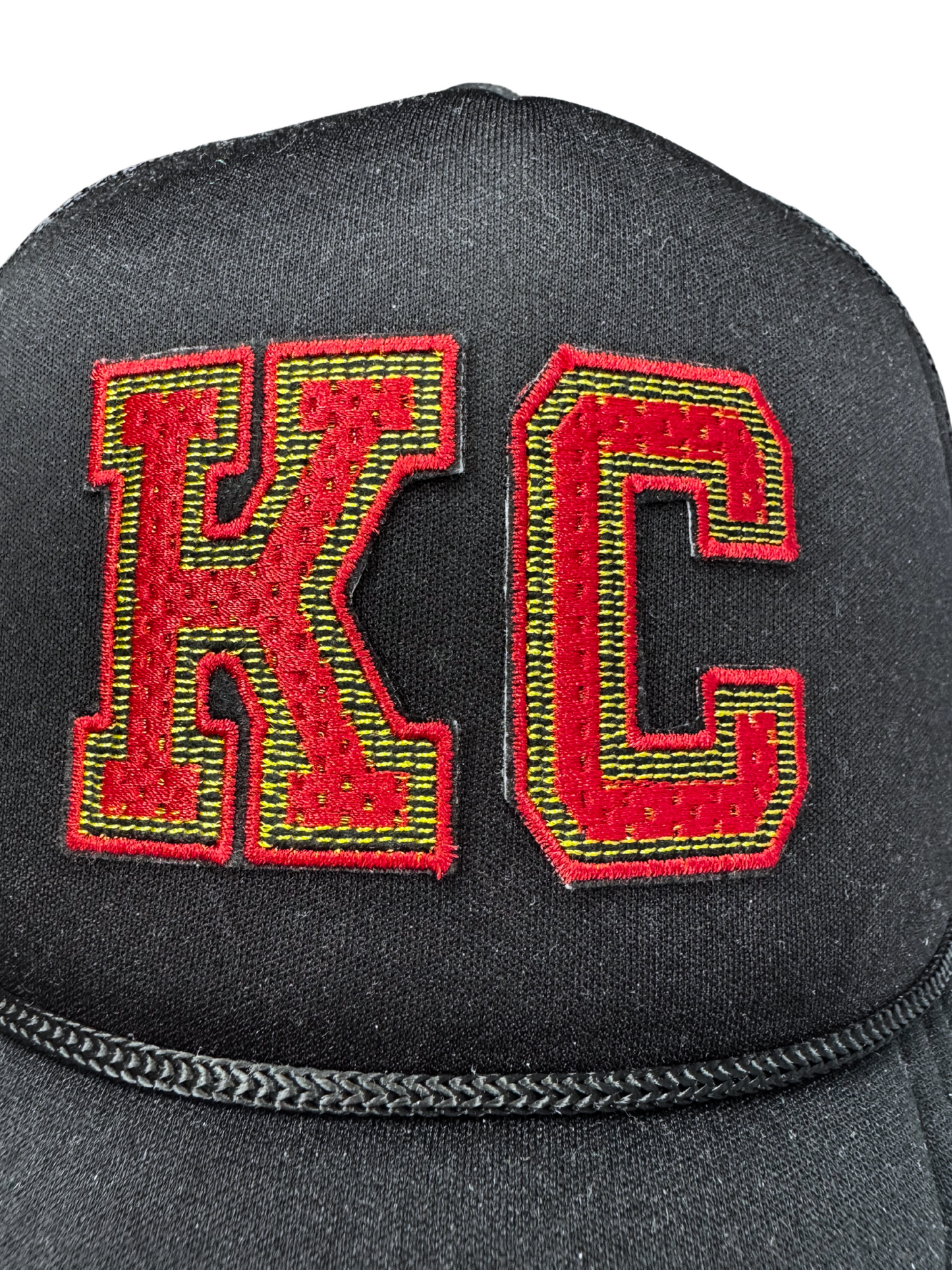 Closeup of red embroidered KC patch with gold and black detailing on black mesh hat