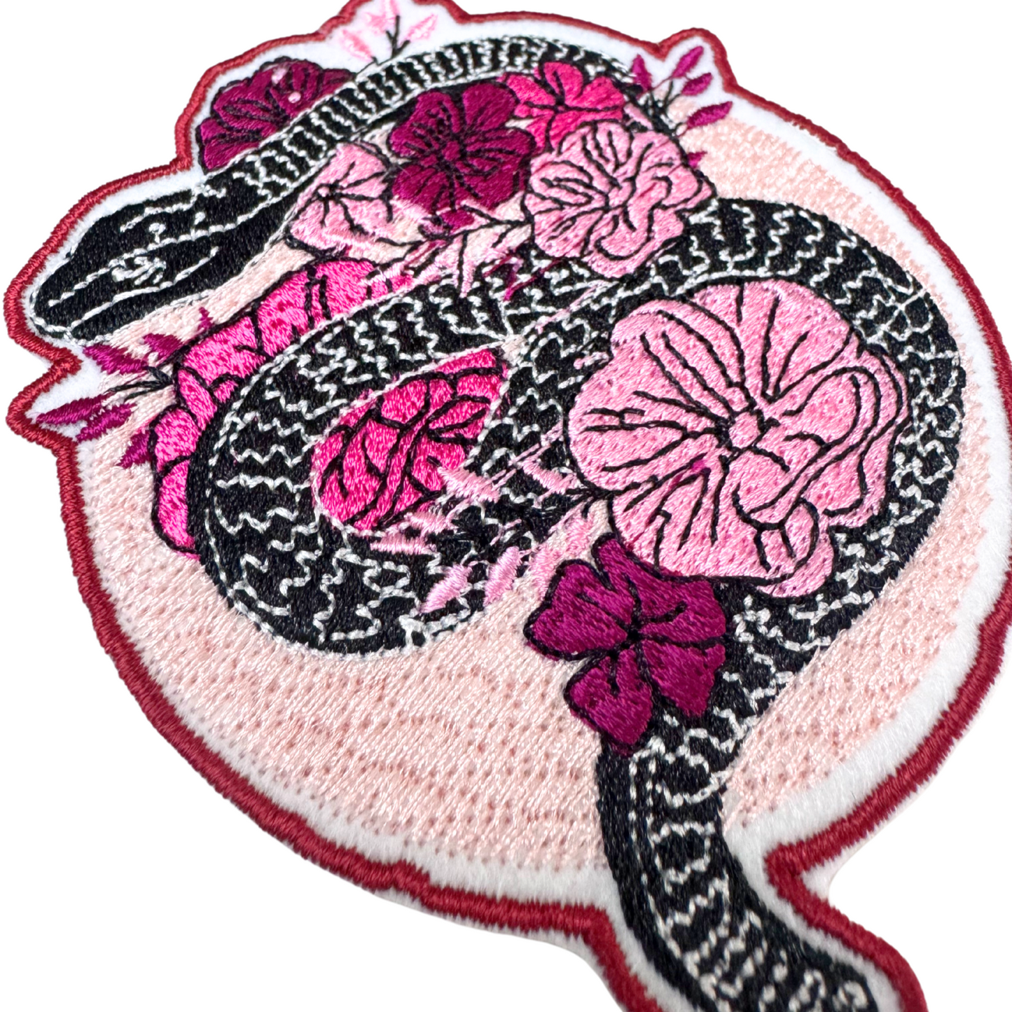 Close-up angled side view of black snake and pink flowers embroidered iron-on patch