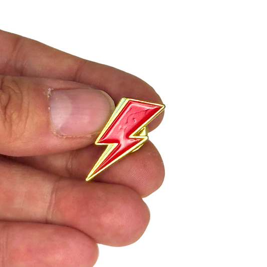 “Red lightning bolt pin shown on fingers for scale”