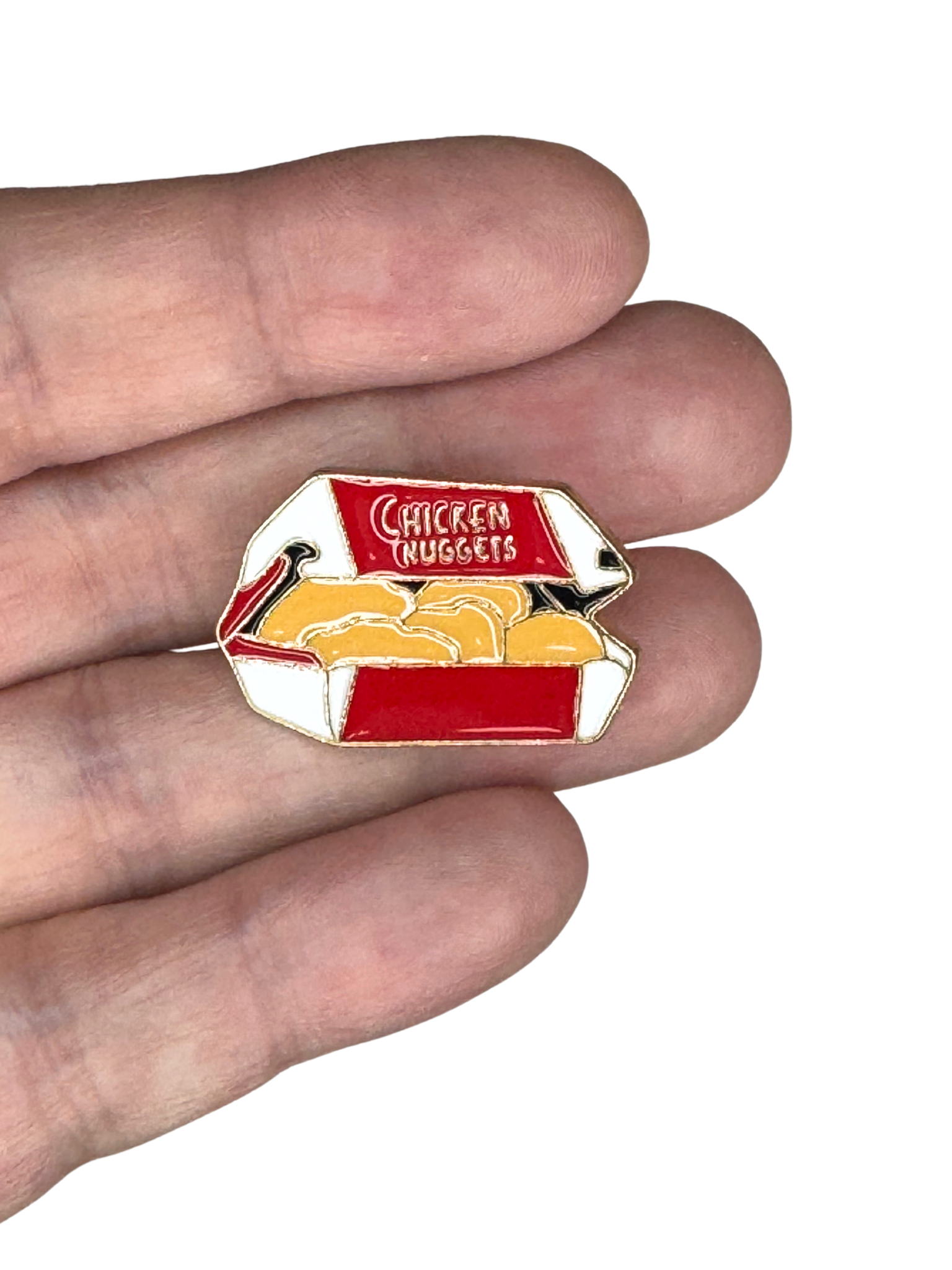 Chicken nuggets enamel pin shown in hand for scale