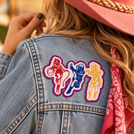 Colorblock Cowgirls embroidered iron-on patch displayed on the back of a denim jacket in a warm retro rodeo lifestyle scene