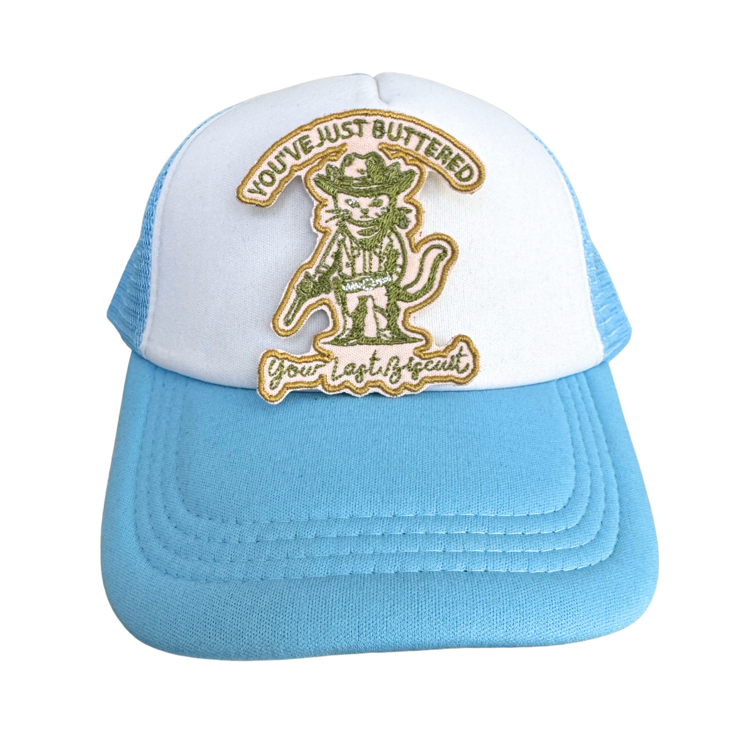 Blue and white trucker hat styled with the "You’ve Just Buttered Your Last Biscuit" green and gold embroidered patch.