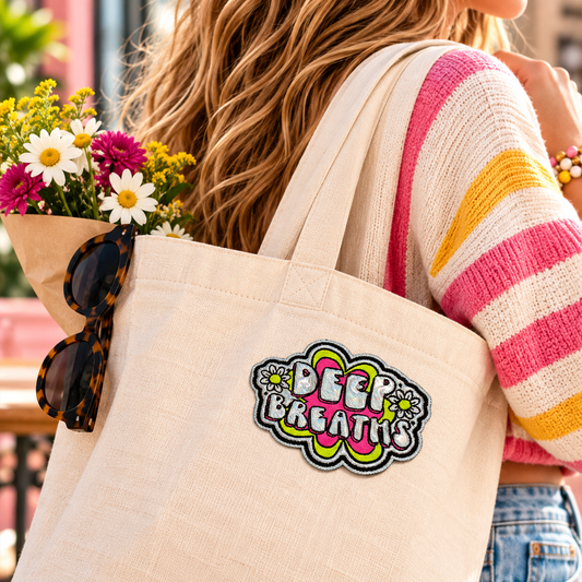 Deep Breaths neon pink and silver holographic embroidered patch on cream canvas tote bag carried outdoors with flowers