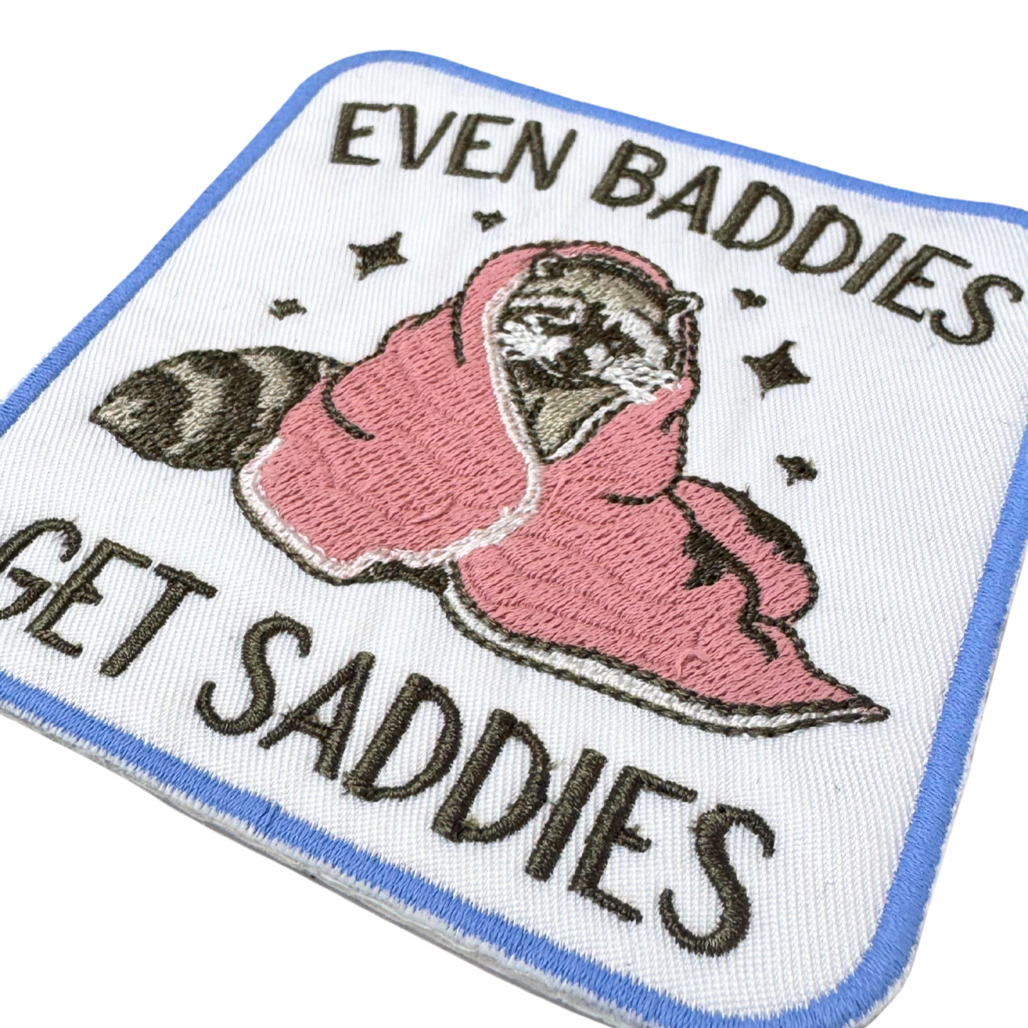Close-up angled view of Even Baddies Get Saddies funny raccoon embroidered patch