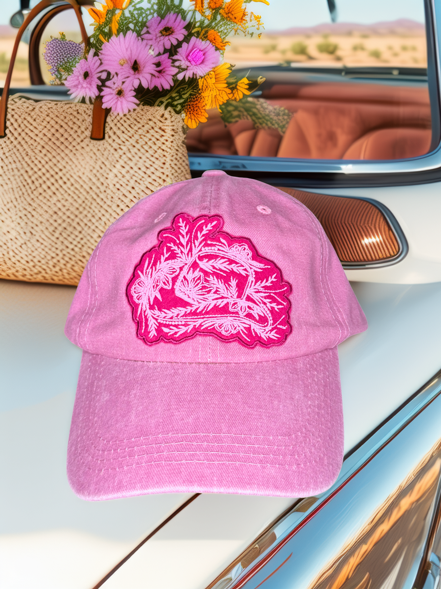 Pink cap with floral design on a car dashboard with flowers in the background