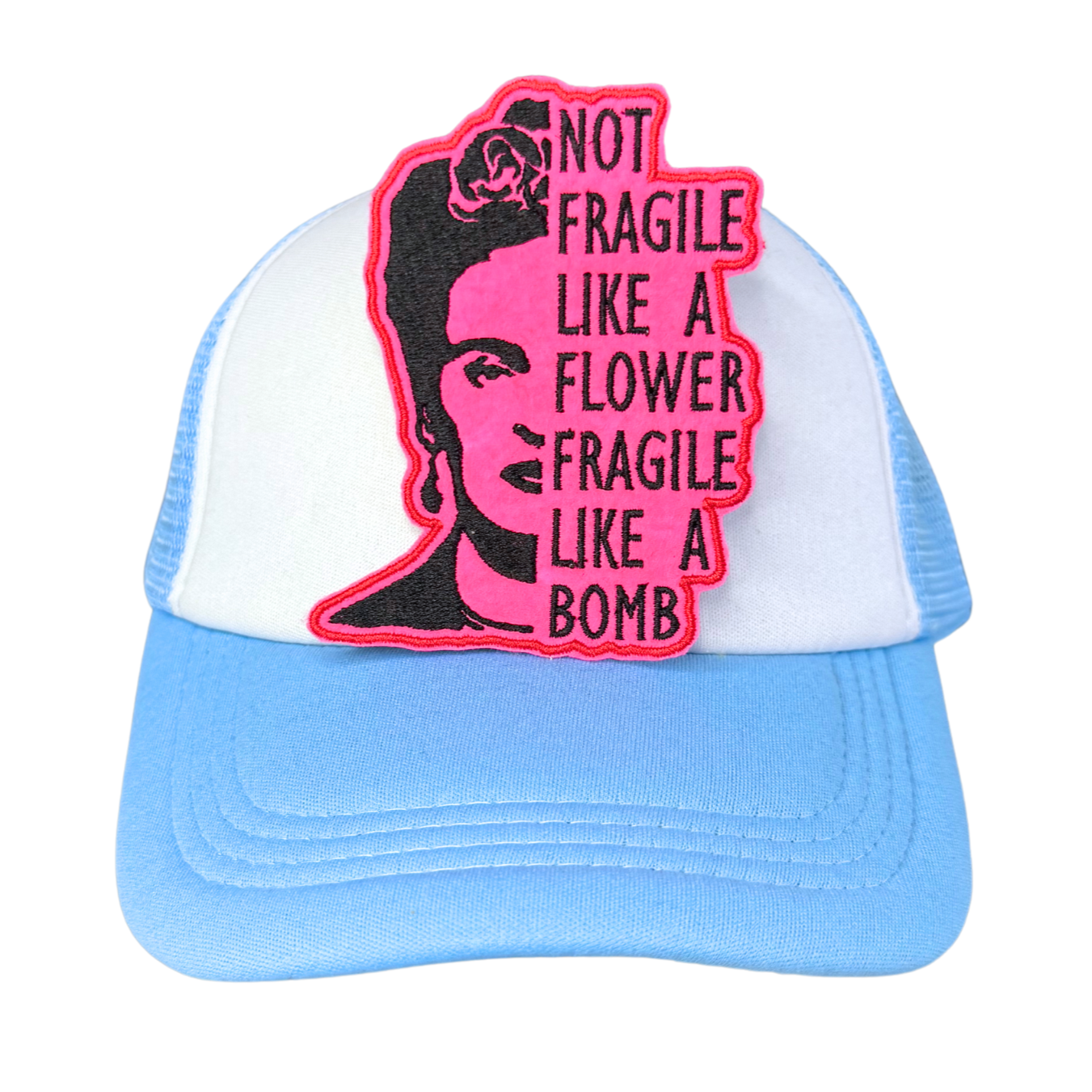 "Blue and white trucker hat with a neon pink embroidered Frida Kahlo patch that reads 'Not Fragile Like a Flower, Fragile Like a Bomb.'"