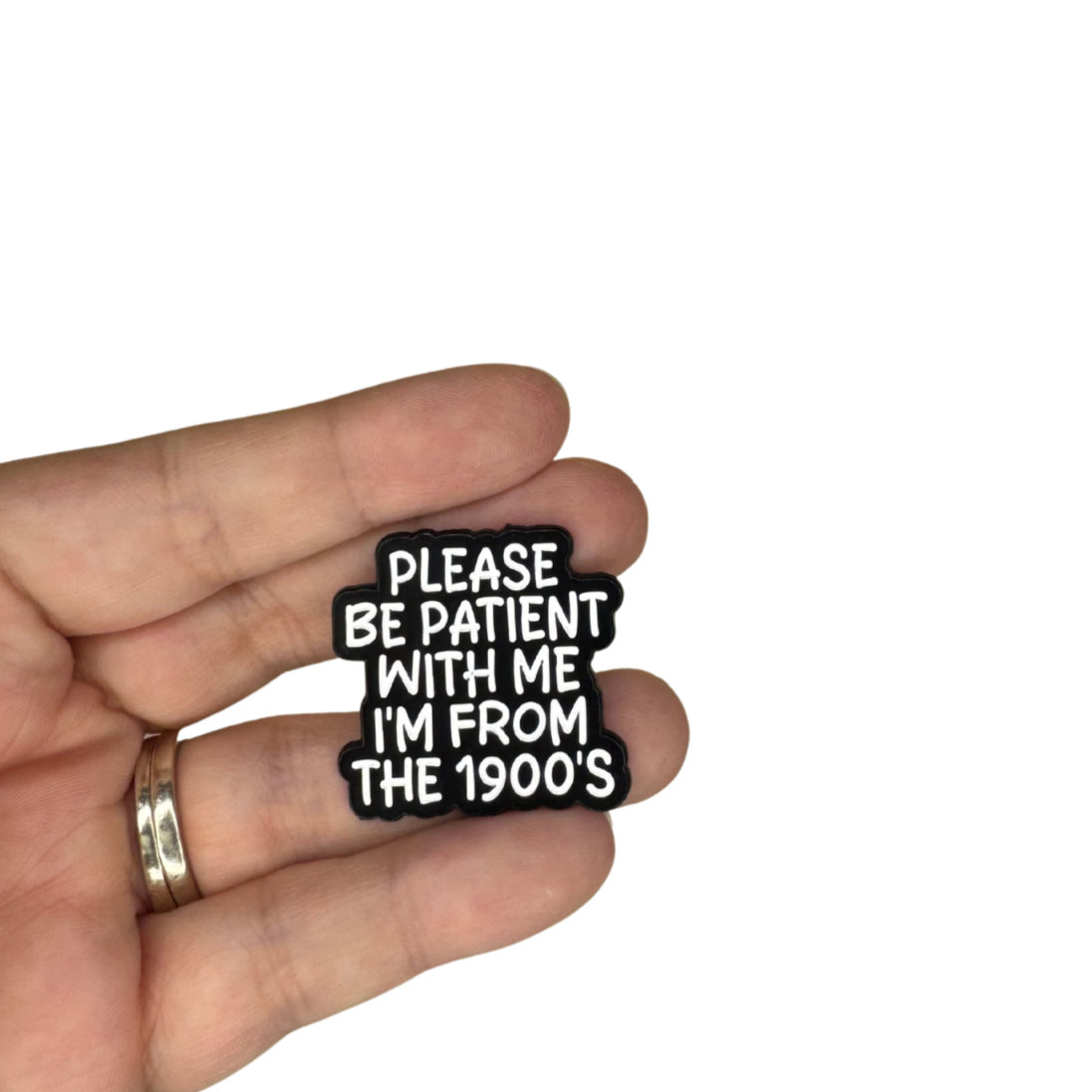 Please be patient with me” enamel pin held in hand for size reference