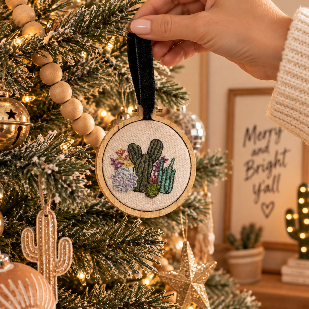 Hand placing hand-embroidered cactus ornament on a southwestern Christmas tree