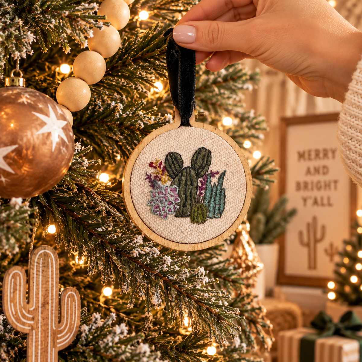 Hand placing hand-embroidered cactus and succulent ornament on a southwestern Christmas tree