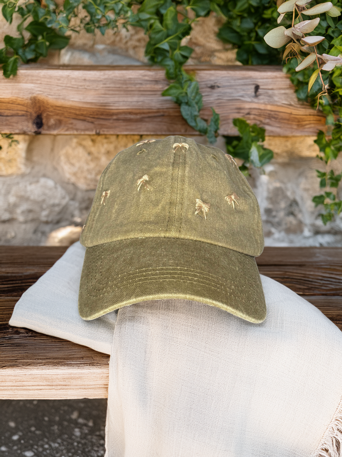 Green cap with embroidered designs on a white towel against a stone wall and greenery background