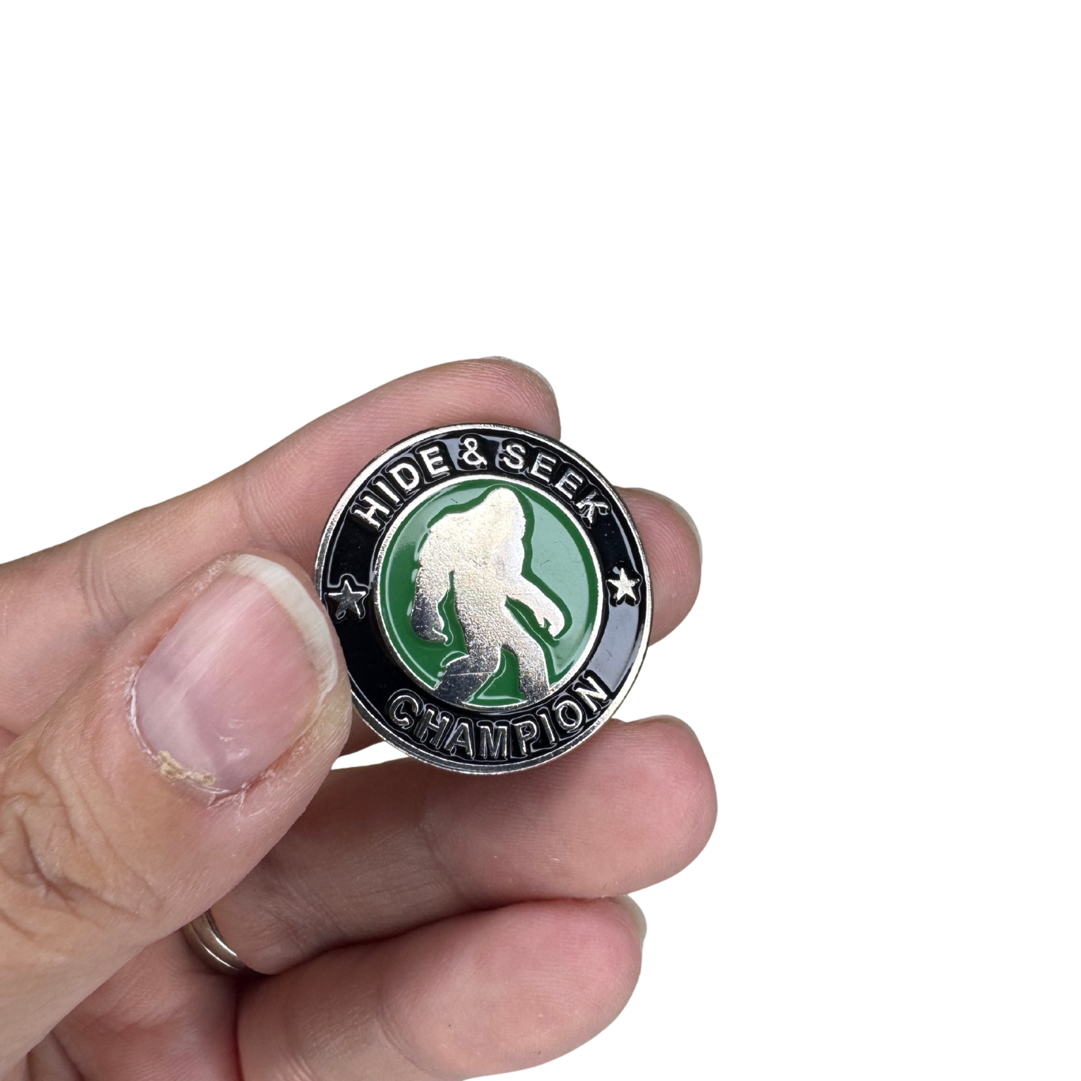 Hand holding Bigfoot Hide & Seek Champion enamel pin