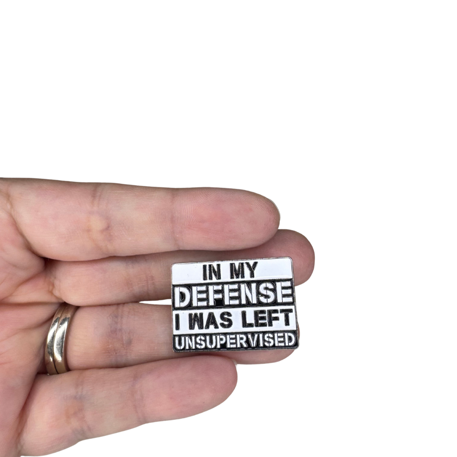 Hand holding “In my defense I was left unsupervised” enamel pin for size scale
