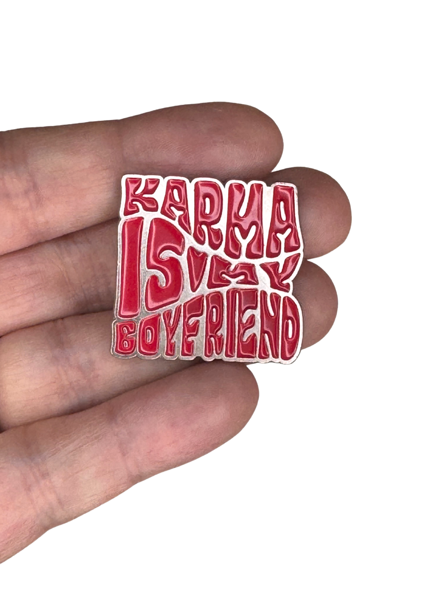 Close-up of the enamel pin held in fingers for scale