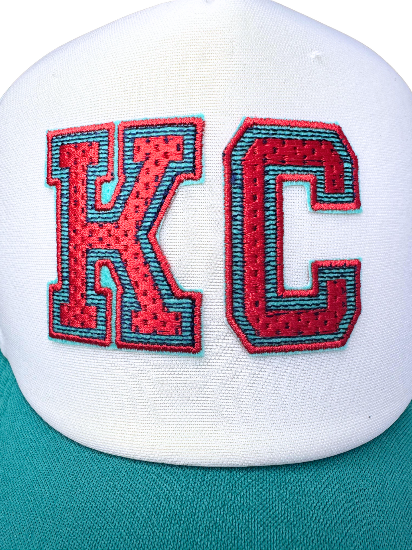 Closeup of varsity-style KC patch in Kansas City Current colors on white foam front of trucker hat