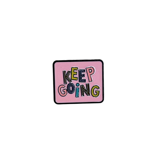 Square pink enamel pin that says “KEEP GOING” in colorful block letters
