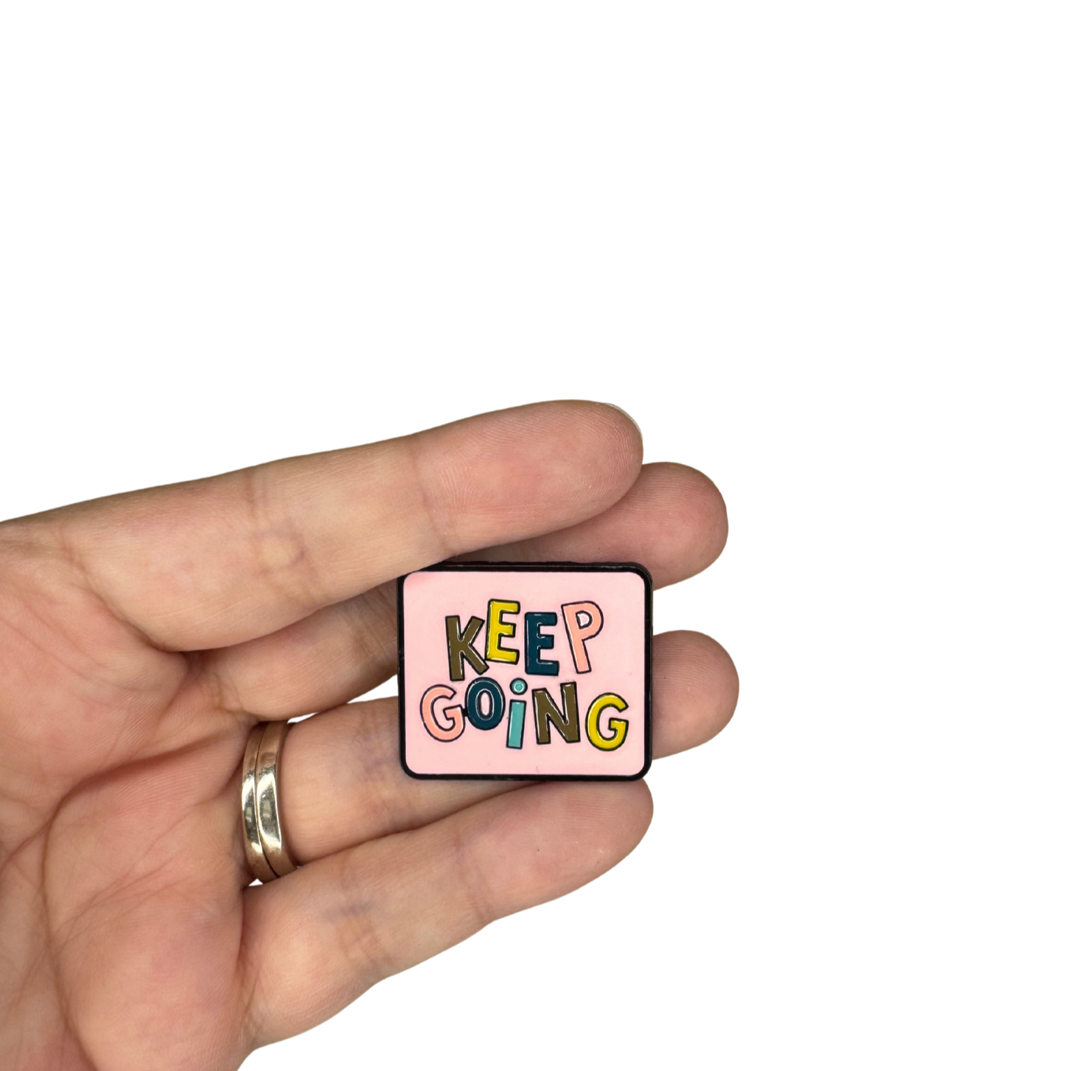 "Keep Going" enamel pin shown in hand for scale