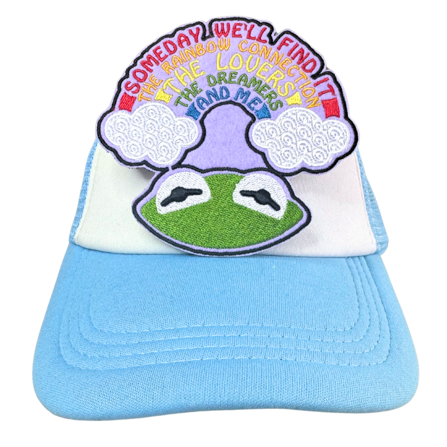Light blue and white trucker hat with an embroidered rainbow dreamer frog patch attached.
