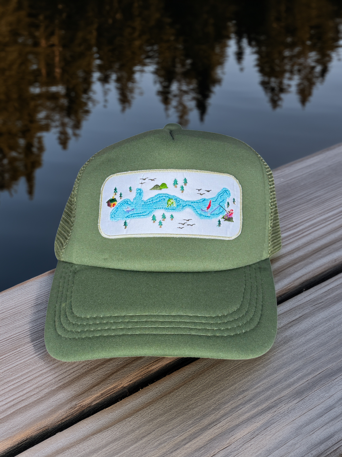 Green cap with a colorful patch on a wooden surface with water and trees in the background