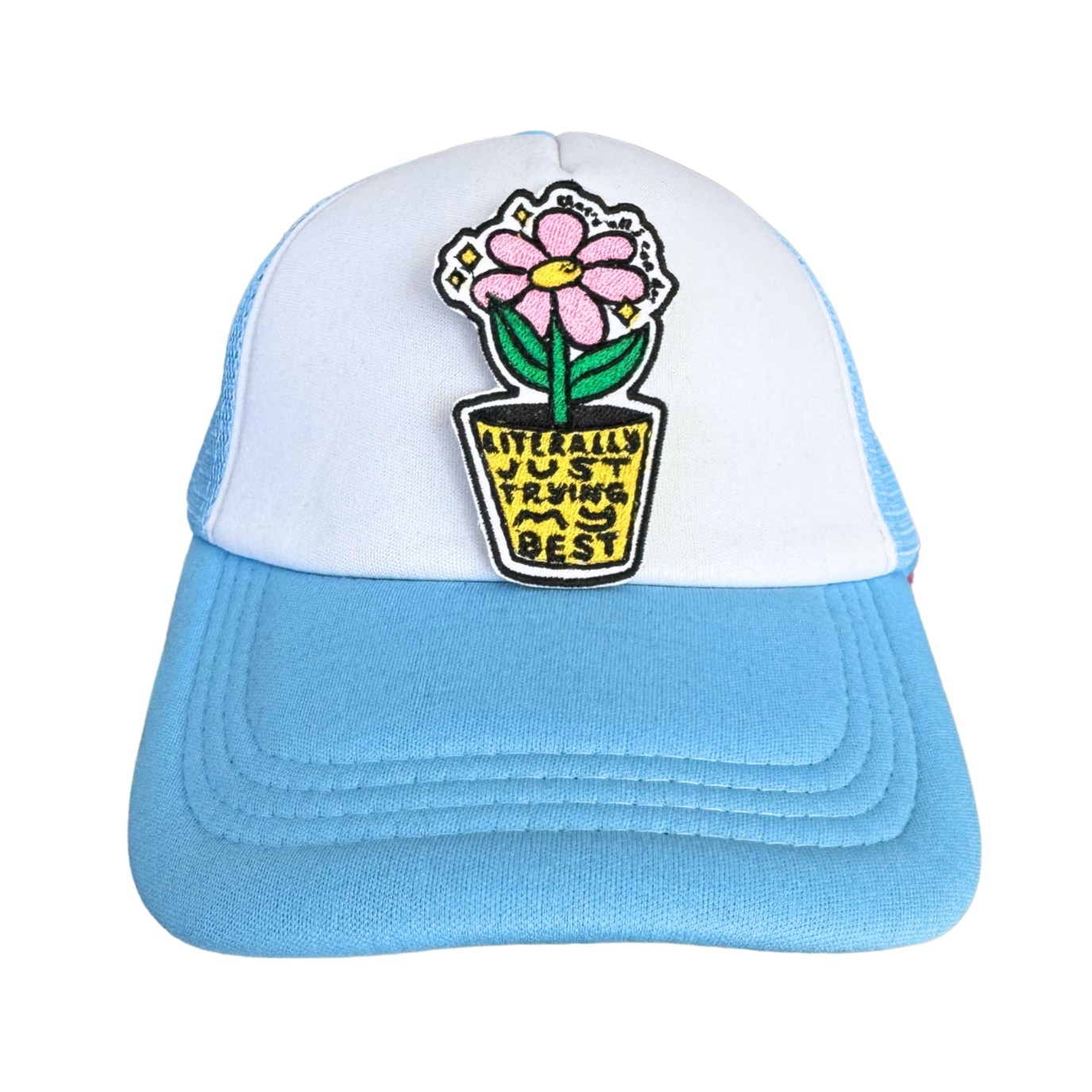 A trucker hat with a white front panel and light blue brim, featuring the "Literally Just Trying My Best" embroidered patch attached to the front.