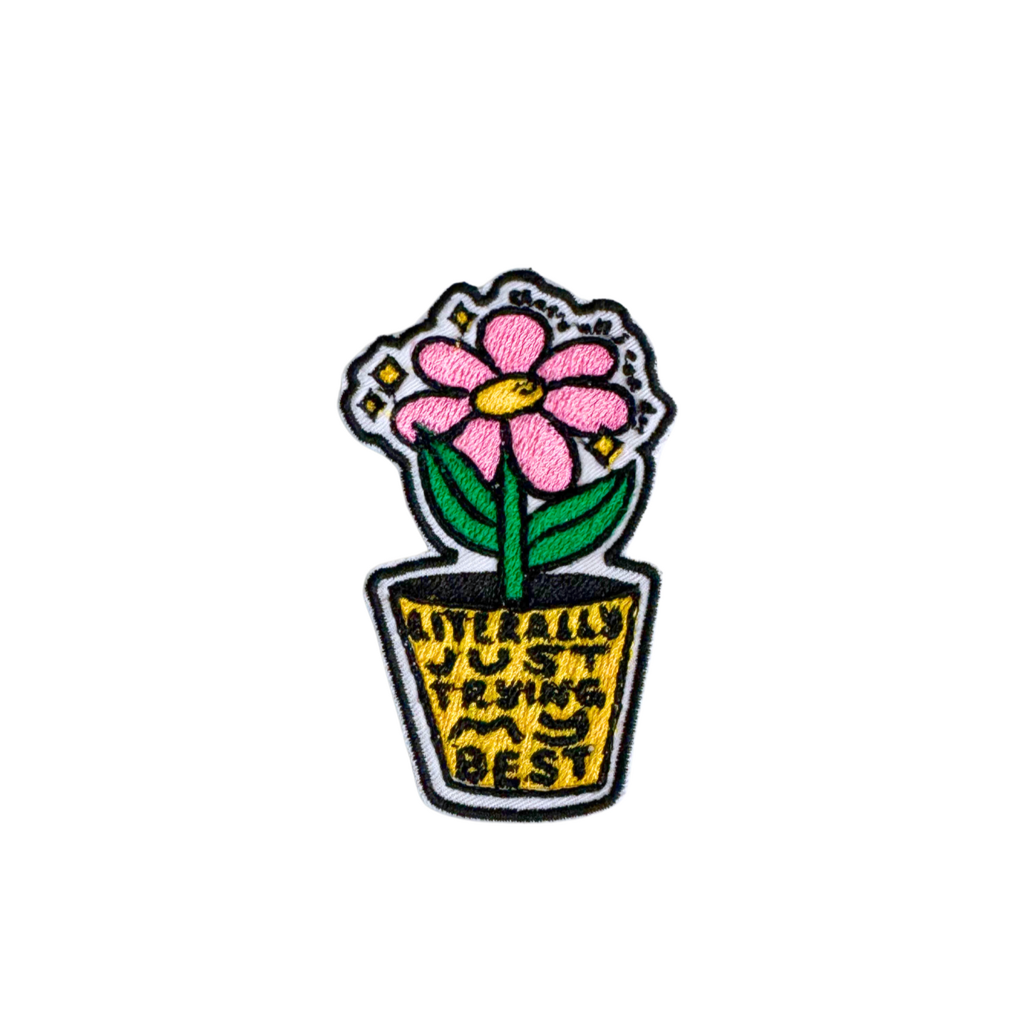 A close-up of an embroidered iron-on patch featuring a pink flower in a pot with the words "Literally Just Trying My Best" in black and yellow embroidery.