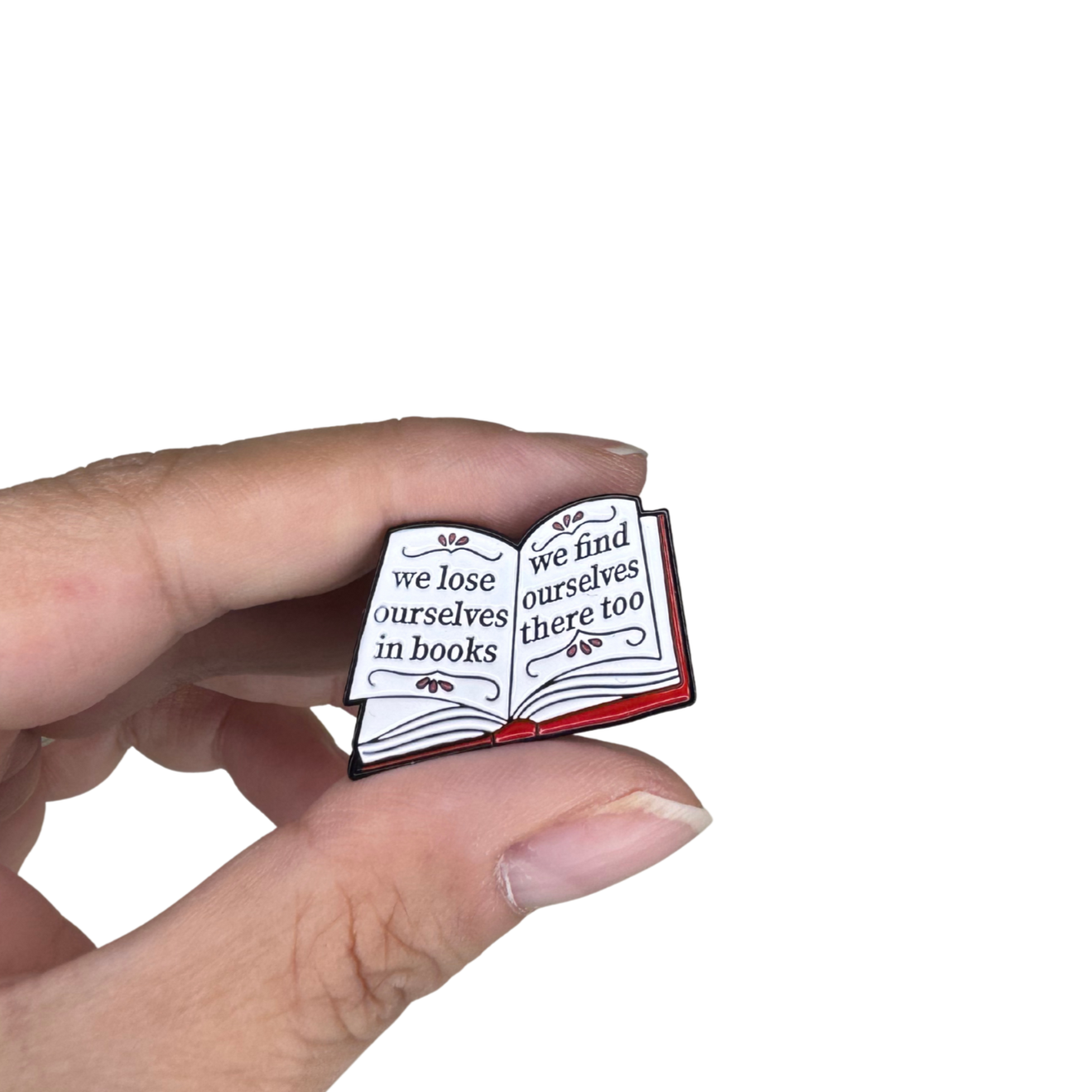Close-up of book-themed enamel pin held between fingers for scale