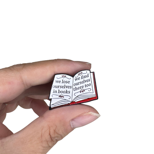 Close-up of book-themed enamel pin held between fingers for scale