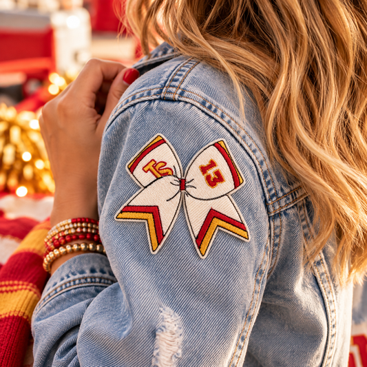Lucky 13 red and gold Chiefs Swiftie bow embroidered patch worn on the sleeve of a light-wash denim jacket