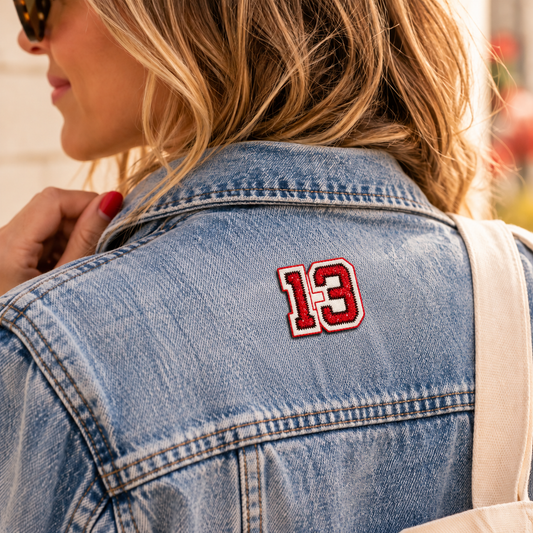 Small red and white embroidered number 13 patch worn on the upper back of a denim jacket