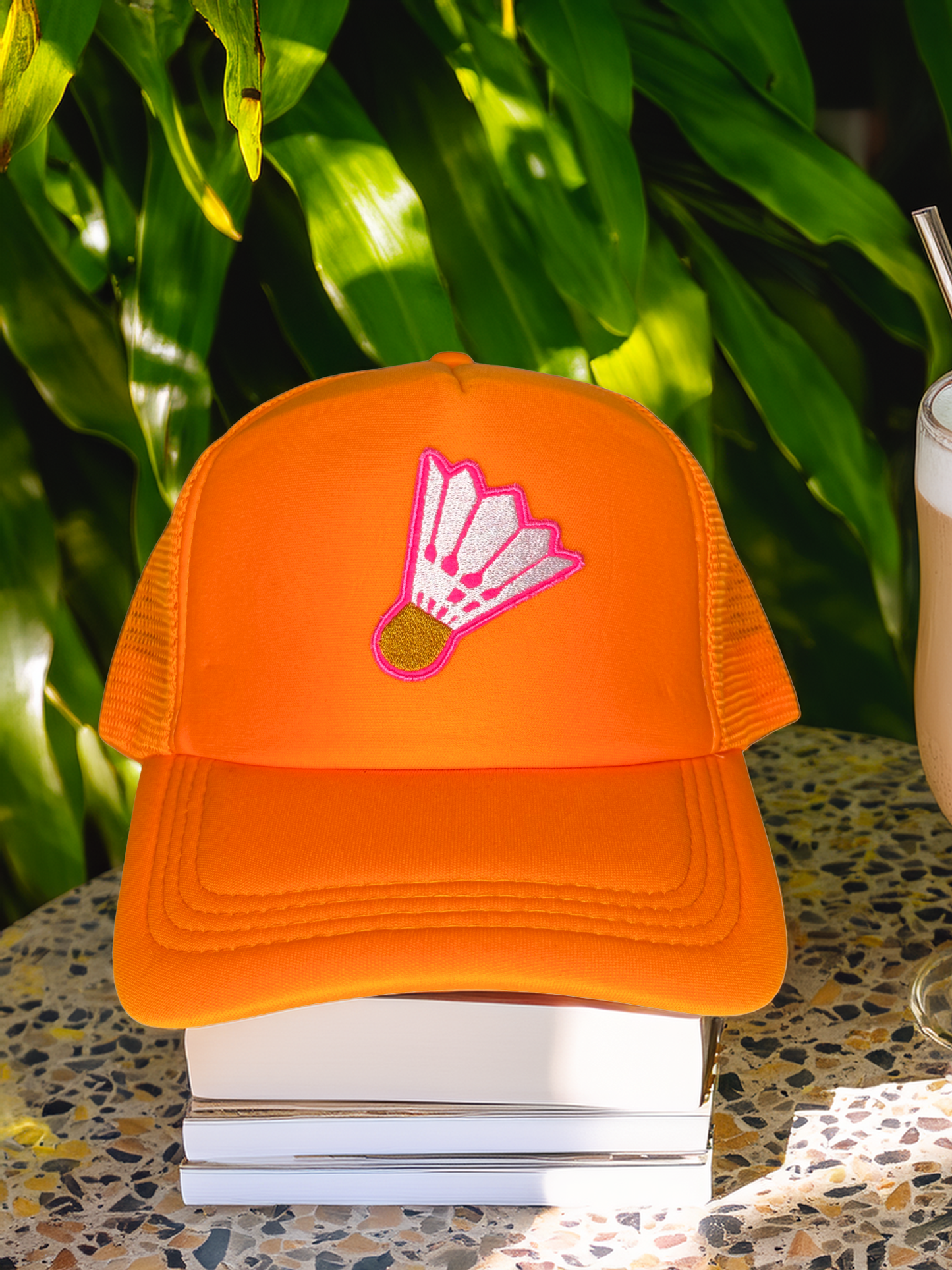 Orange cap with a badminton shuttlecock design on a stack of books with a blurred background