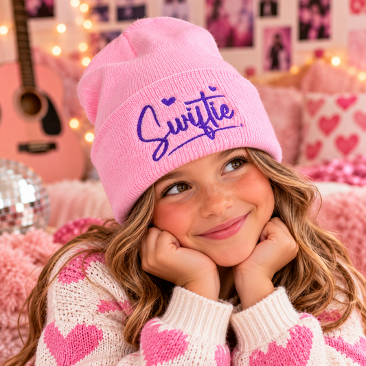 Young girl wearing the pink Swiftie embroidered youth beanie with purple script and heart details.