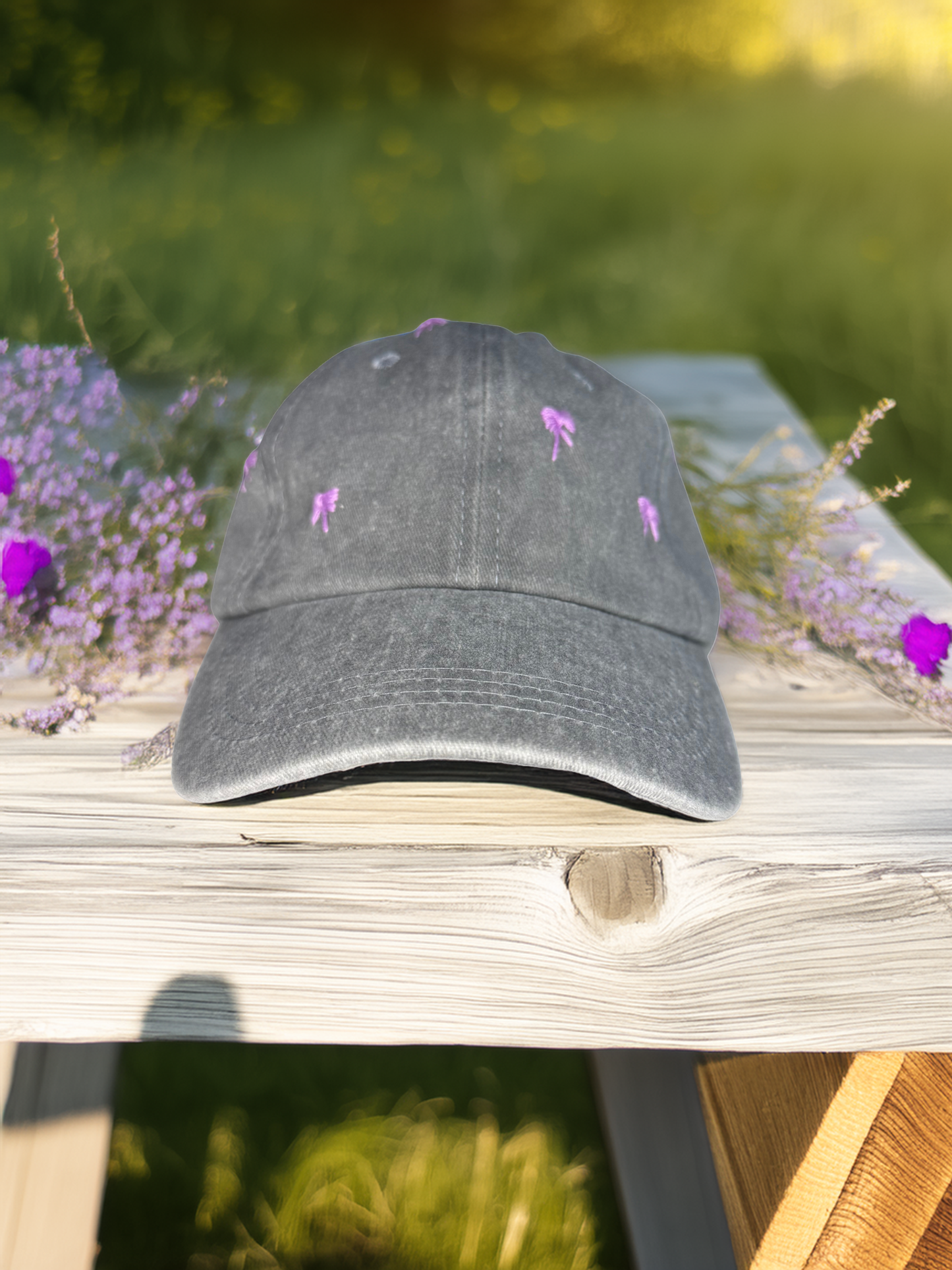 Gray cap with embroidered purple bows on a wooden surface with blurred greenery in the background