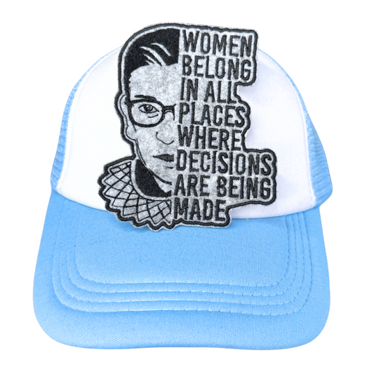 "Blue and white trucker hat with an embroidered RBG patch that reads 'Women belong in all places where decisions are being made.'"