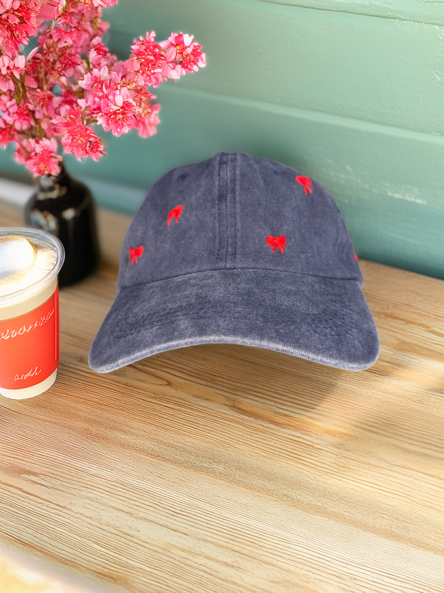 Blue cap with red patterns on a wooden surface next to a candle and pink flowers.