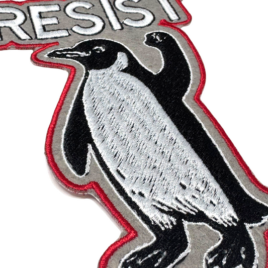Close-up angled view showing embroidery texture of RESIST penguin patch