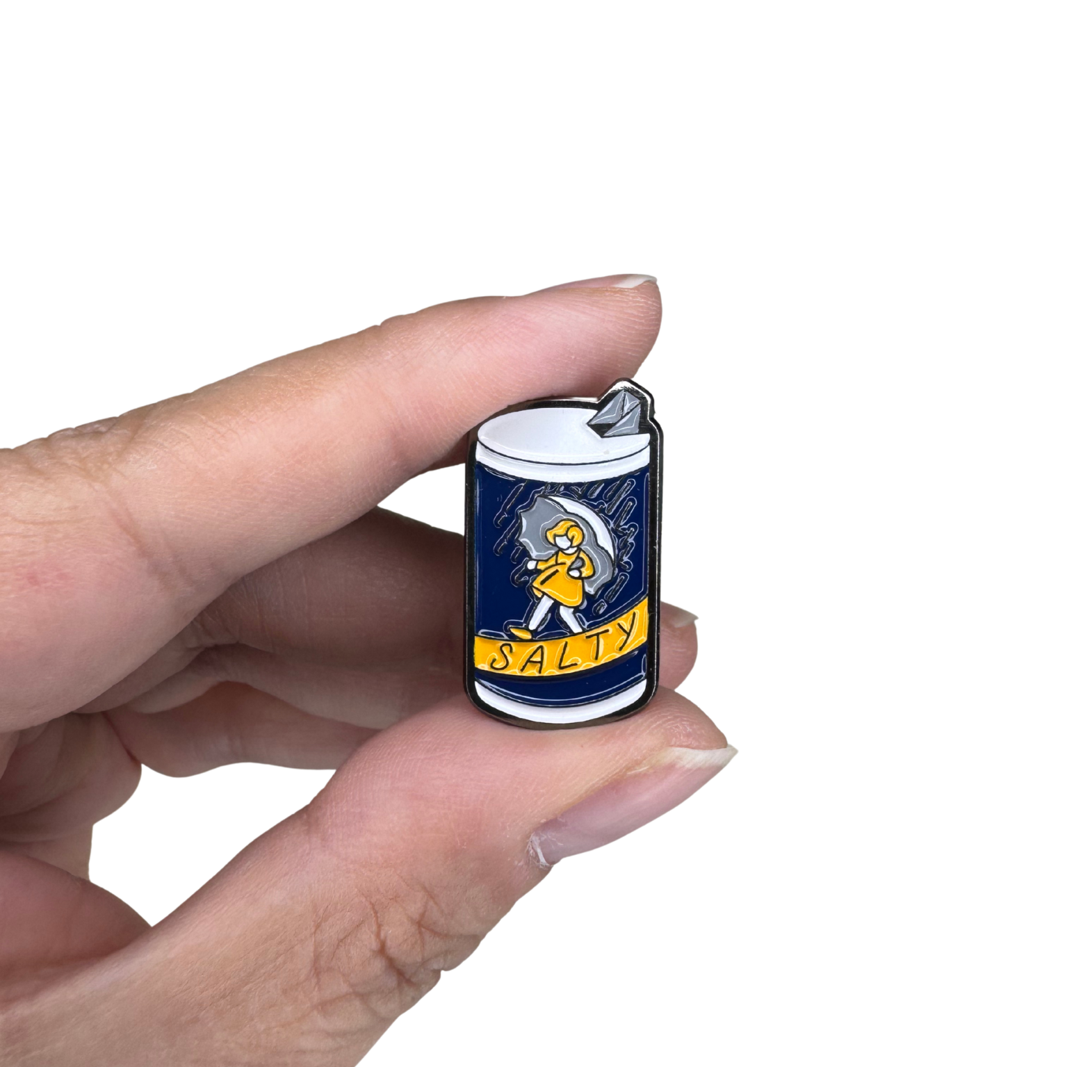 Salty enamel pin held between fingers for scale