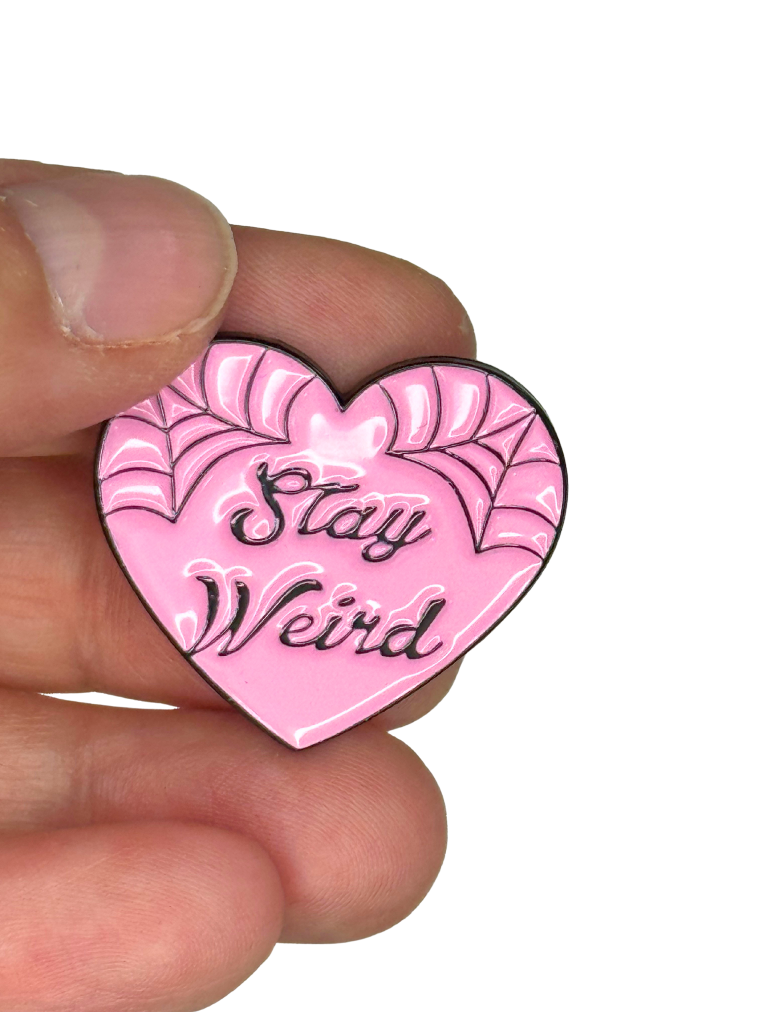 “Stay Weird pin shown on fingers for scale”