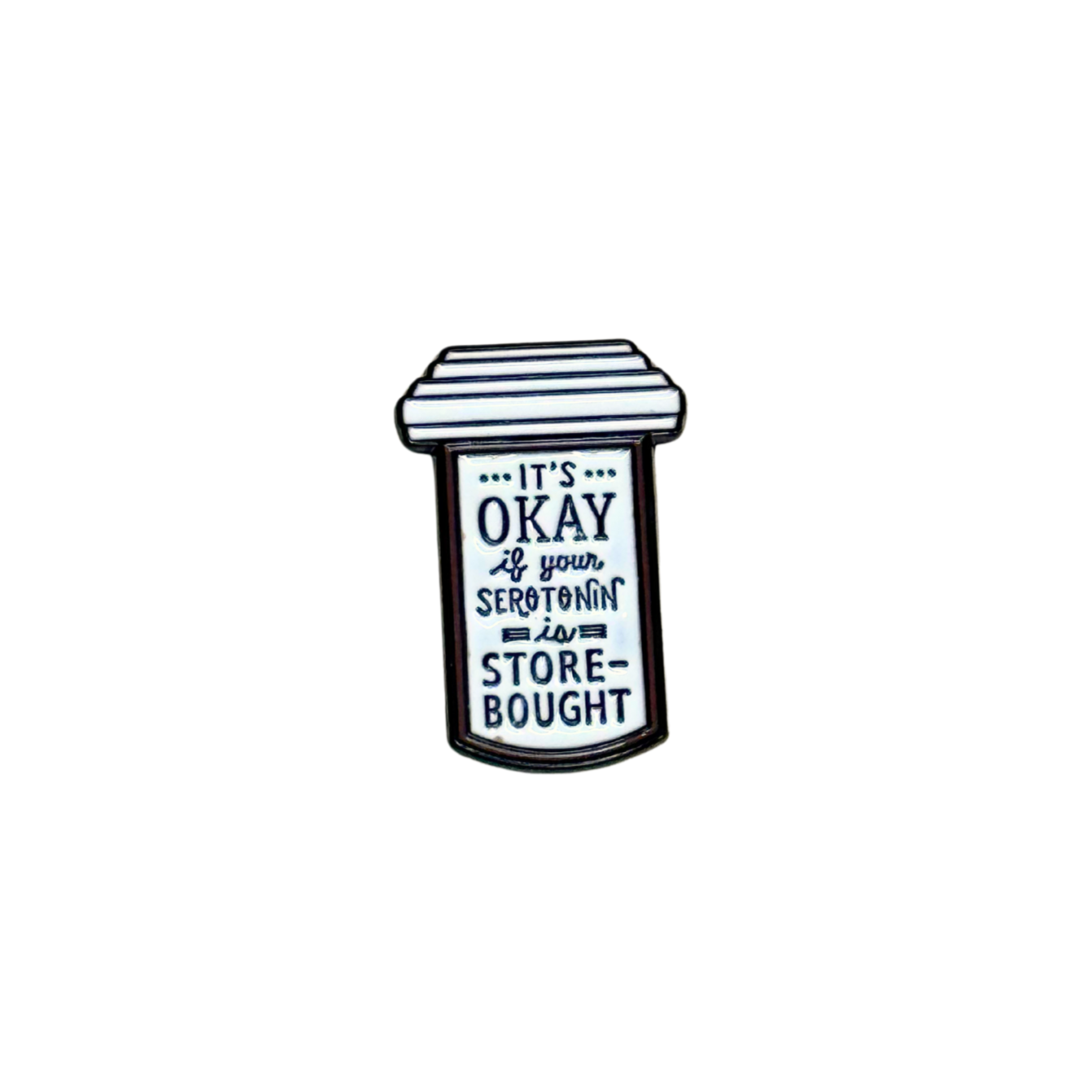 Black and white enamel pin shaped like a prescription bottle with text that reads “It’s okay if your serotonin is store-bought”
